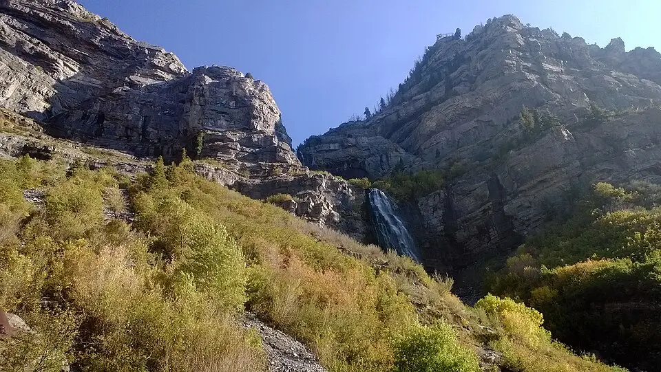Bridal Veil Falls seen from a trail below the cliffs in Provo Canyon, with fall-colored brush on the slope
