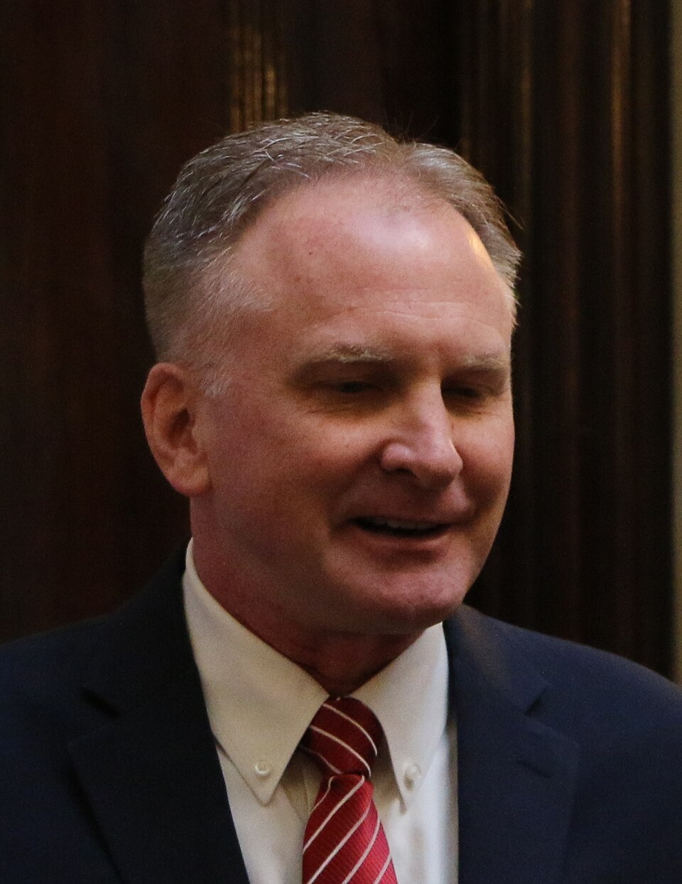 Craig Hall, wearing a dark suit and red striped tie, sits in the Utah House chamber.