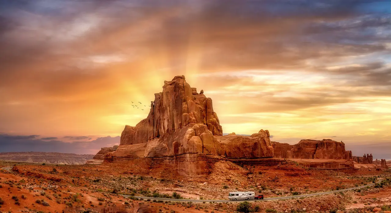 Red rock formations in Arches National Park at sunset, with a motorhome on the road below